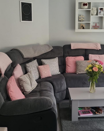 Cozy living room featuring a gray corner sofa adorned with pink cushions and a small coffee table with flowers.