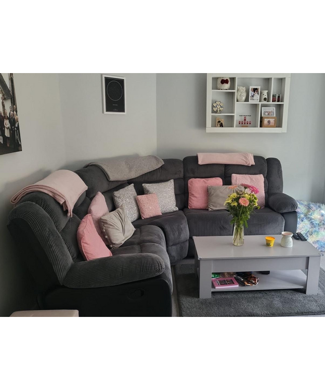 Cozy living room featuring a gray corner sofa adorned with pink cushions and a small coffee table with flowers.