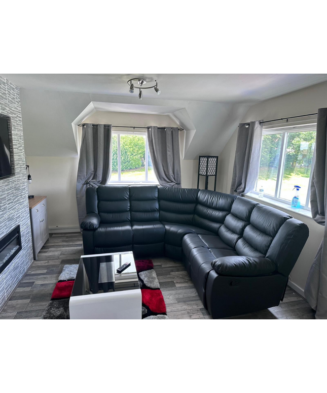 Black leather Roma recliner corner sofa in a bright living room with windows and stylish decor.