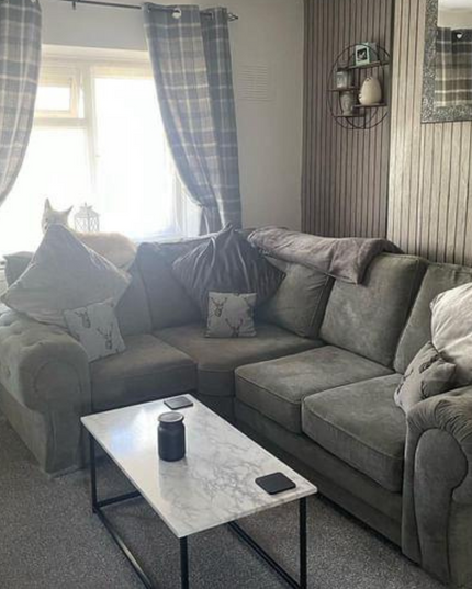 Cozy living room featuring a grey corner sofa with cushions, a marble-top coffee table, and plaid curtains.