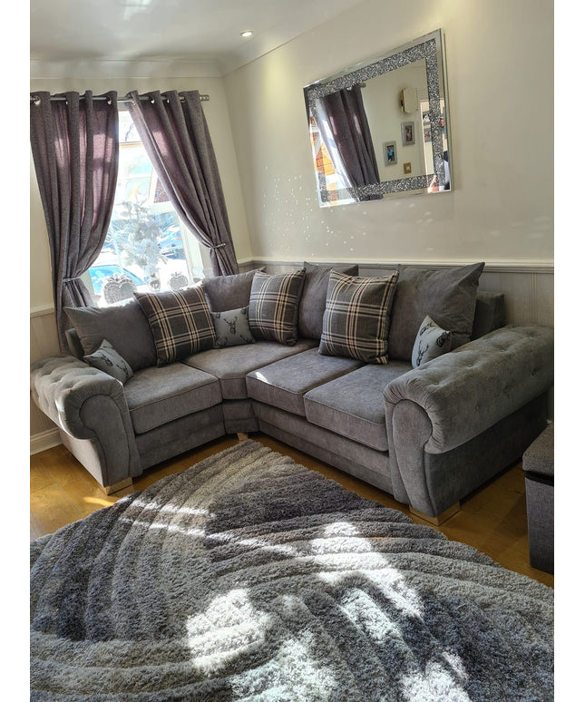 Verona corner sofa in grey with plaid cushions, placed in a sunlit living room with curtains and a decorative mirror.