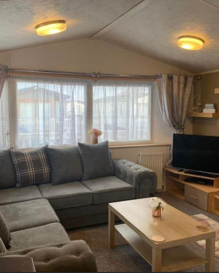 Cozy living room with a grey corner sofa, a coffee table, and a TV beside a warm fireplace.